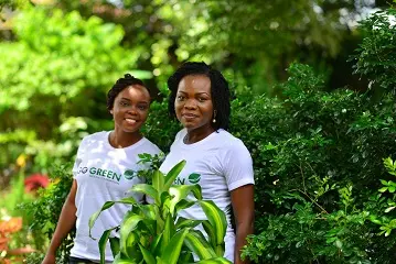 Two volunteers standing among plants in Go Green Nigeria Foundation shirts